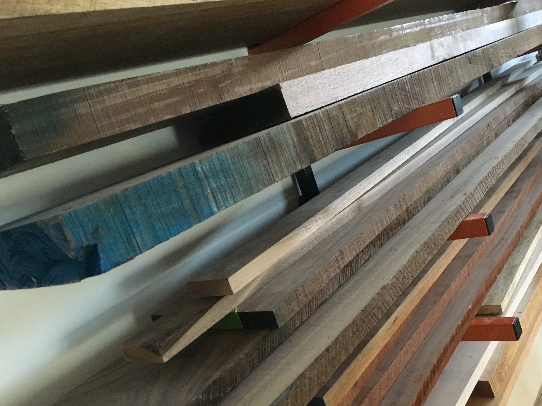 Hardwood boards stacked on a wall rack, including a blue-dyed piece and figured maple