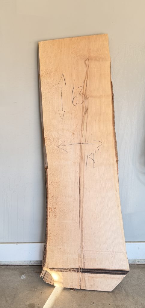 Hard maple live-edge slab standing upright in the shop